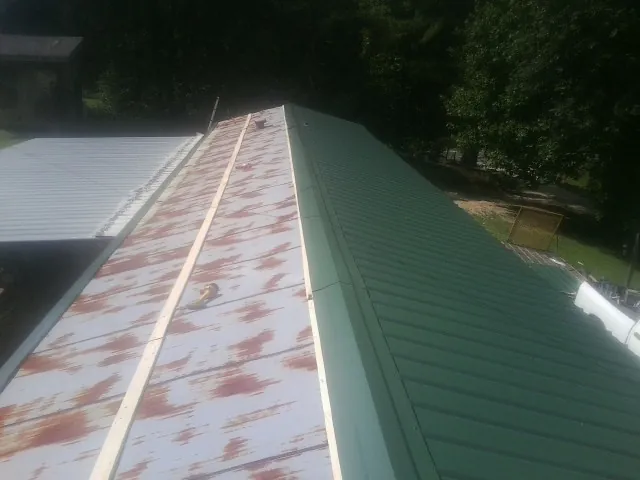 Old rusted panels beside newly installed green metal roofing — Wind Damage Roof Repair by Roofing Brothers in Maynard