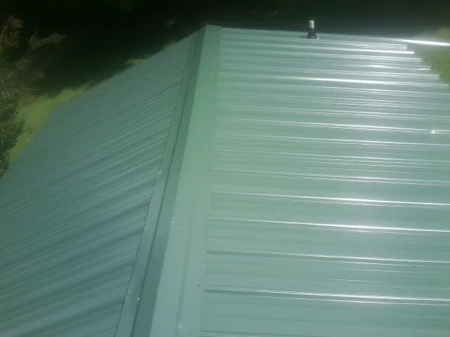 New green metal panels meeting at the ridge of a roof — Flat Roof Repair work by our crew in Maynard