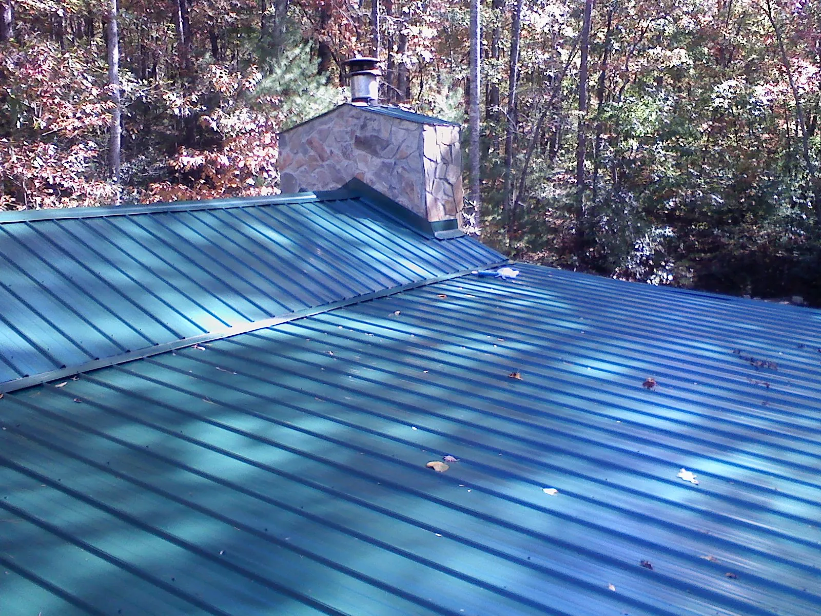 New green metal roof and stone chimney surrounded by autumn woods in Maynard